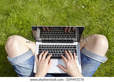 Man using laptop on a summers day sitting outside on grass