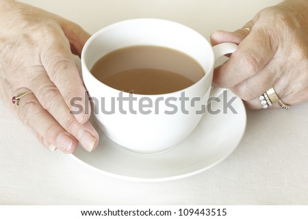 Senior woman holding a cup of tea on white table cloth