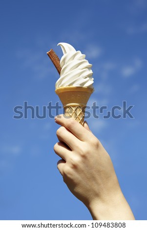 Ice cream cone with chocolate flake being held in the air against a blue summer sky