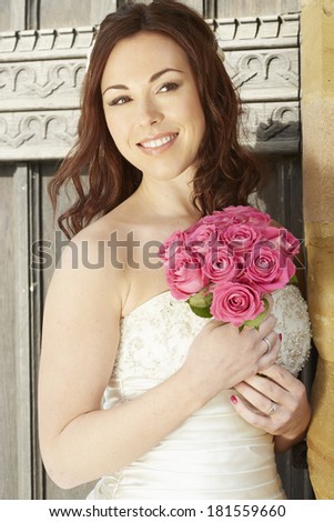 Female bride holding a wedding bouquet of pink roses in church door smiling