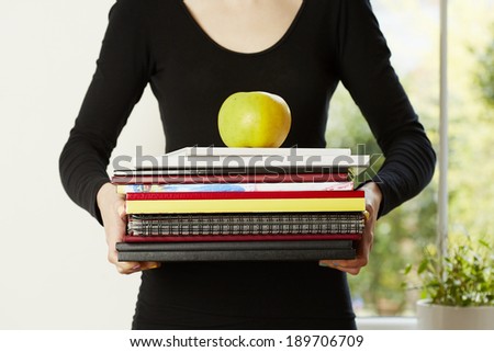 Female hands holding pile of books with apple on top. Student education concept