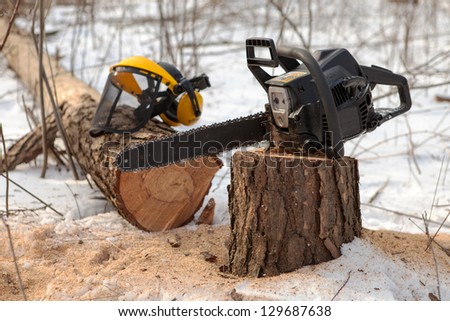 Chain saw on pine stump and protective visor with hearing protection on the fallen tree in winter