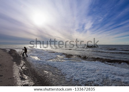 A man with stick walks around the frozen Baltic sea coast landscape with beautiful sky and sun
