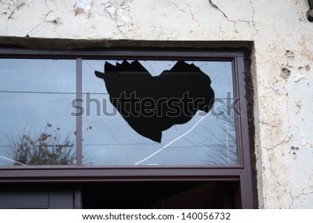 The shape of an angular heart in the broken glass of the window over the outside door of the house in the street