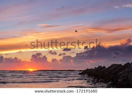 Spectacular colorful seascape of Baltic sea at sunset after storm with breakwater in foreground leading to sun at horizon