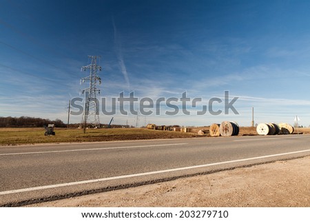 High voltage electricity pylon with workers on it building up a new power line on blue sky background with clouds