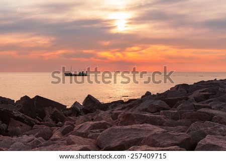 Fishing boat leaving harbor at stunning cloudy sunset with breakwater made of granite