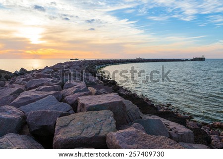 Breakwater with gates and fishing boat leaving harbor at dramatic cloudy sunset