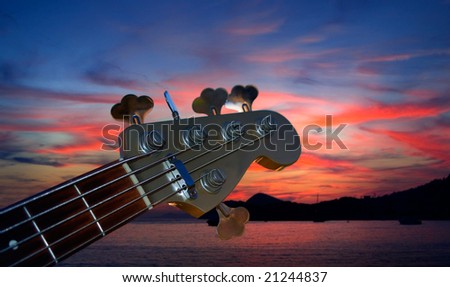 Bass guitar play in the dusk on the red sky and sea