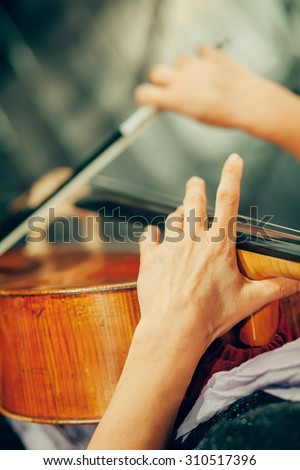 Symphony orchestra on stage, hands playing violin.\
Shallow depth of field, vintage style.
