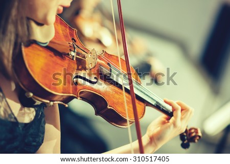Symphony orchestra on stage, hands playing violin.\
Shallow depth of field, vintage style.