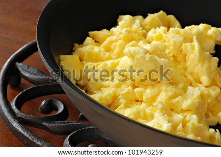 Freshly prepared scrambled eggs in healthy, eco friendly, ceramic nonstick skillet on trivet.  Macro with shallow dof.