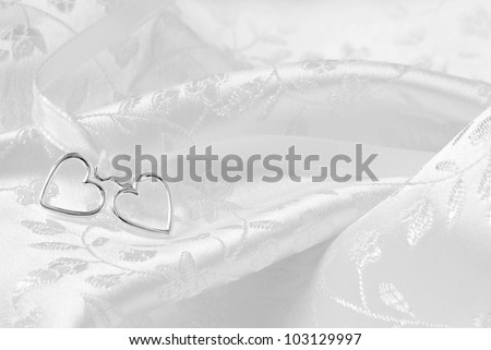 Wedding background of two silver hearts joined together with ribbon on elegant white satin brocade fabric.  Macro with extremely shallow dof.