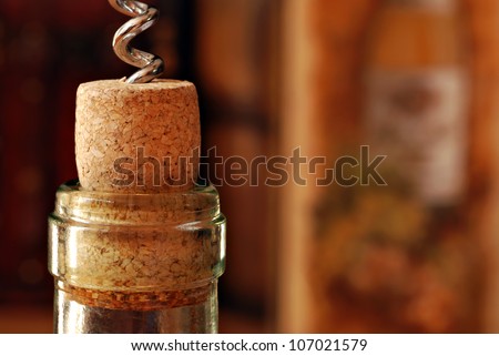 Wine bottle with corkscrew and partially removed cork.  Wine related decor in soft focus in background.  Macro with shallow dof.