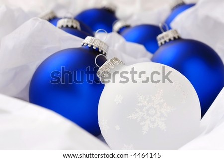 glass Christmas ornament with snowflake design nestled in white tissue paper with blue ornaments.