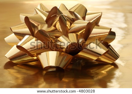 Shiny gold gift bow on gold metallic wrapping paper with reflected backlighting