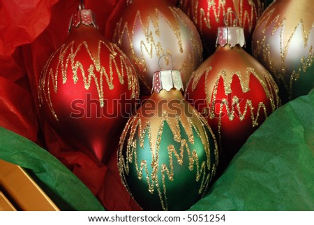 Decorative glass Christmas ornaments in a gold box with green and red tissue paper