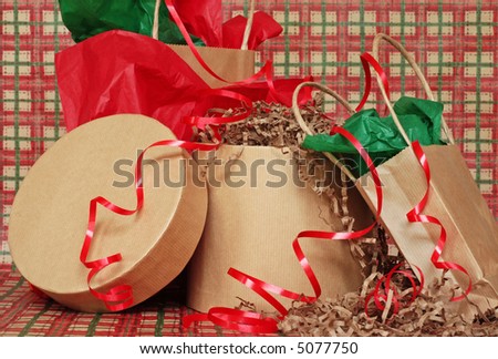 Christmas gifts in brown paper bags and boxes with green and red tissue paper and ribbon on a sweep of country plaid wrapping paper.