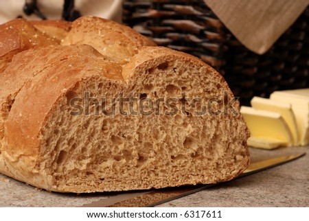 Bread and Butter.  Close-up of sliced, 9-grain, Italian Bread with knife on ceramic cutting board.  Bread basket and sliced butter in soft focus in the background.