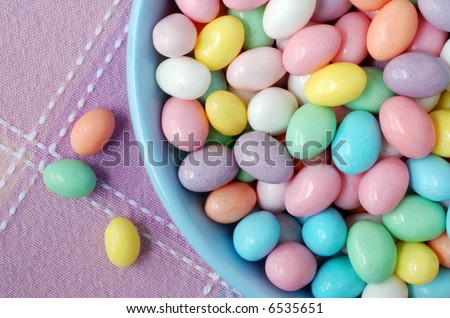 Close-up image of pastel colored jelly beans in a blue ceramic bowl with 3 additional jelly beans laying on the tablecloth.