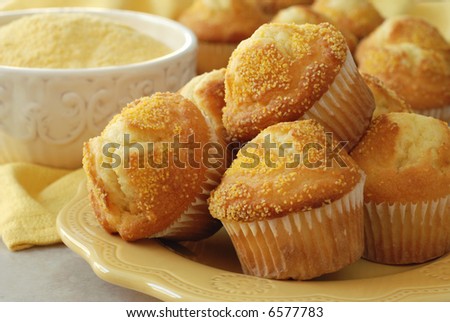 Close-up of corn muffins on plate with bowl of corn meal and additional muffins in the background.  Shallow dof