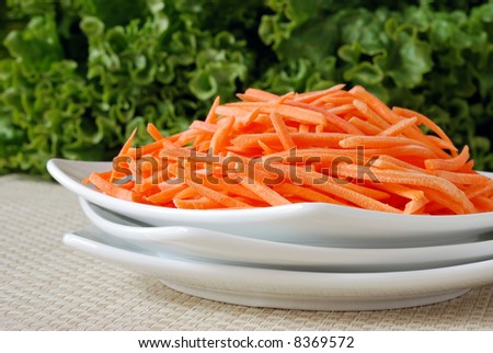 Fresh, shredded carrots with leaf lettuce in the background.  Close-up with shallow dof