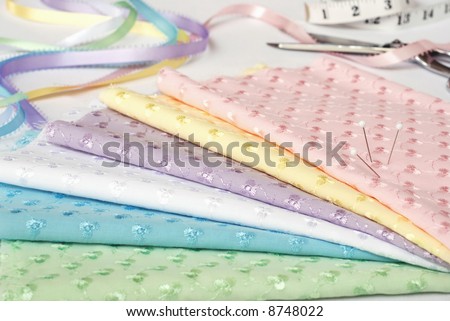 Sewing still-life with embroidered eyelet fabric in spring pastel colors.  Ribbon, scissors, and tape measure visible in the background.  Extremely shallow dof
