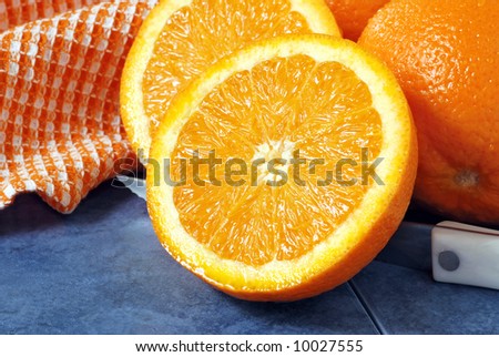 Freshly sliced orange with knife on blue ceramic tile.  Whole oranges and color coordinated dish towel in background.  Close-up with shallow dof.