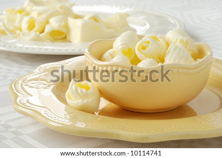 Creamy butter curls in a decorative dish with bits and pieces of stick butter visible in the background.  Close-up with extremely shallow dof