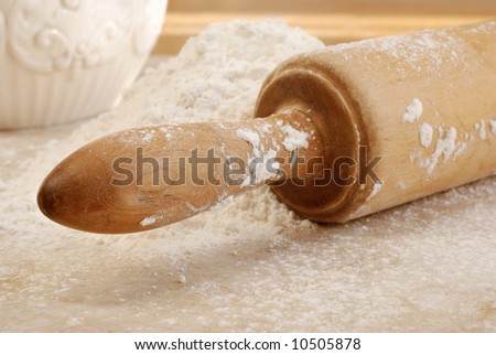 Vintage wooden rolling pin with flour on sunlit countertop.  Close-up with selective focus on handle.  Shallow dof.