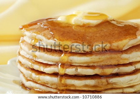 Golden pancakes with butter and warm maple syrup.  Close-up with extremely shallow dof and soft yellow background.