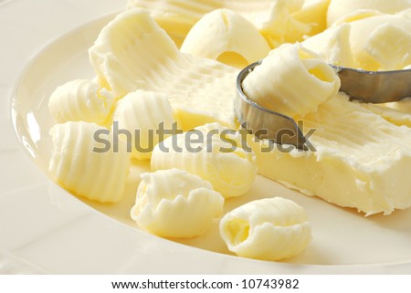 Old-fashioned butter curler with sticks of butter and fresh, creamy curls on a porcelain plate.  Close-up with shallow dof.