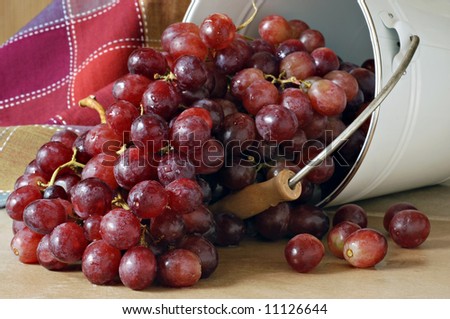 Freshly washed red grapes spilling out of a bucket onto ceramic tile with colorful table linen in the background.  Close-up with shallow dof.