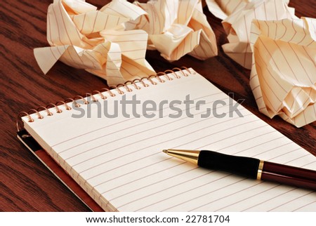 Blank notepad with ink pen on wooden desk.  Crumpled paper in soft focus in background - conceptual image for creative block.