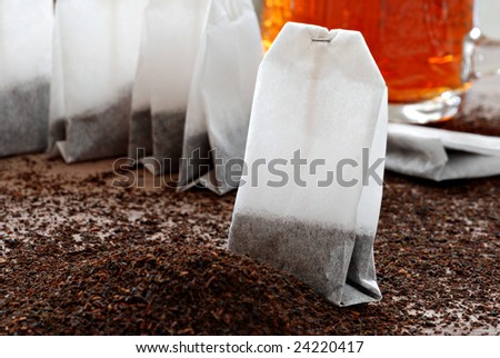 Tea bags and dried tea leaves with  prepared tea in the background.   Macro still life with shallow dof.