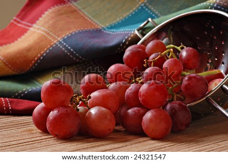 Freshly washed red grapes spilling from metal colander.  Colorful table linen as background.  Macro with extremely shallow dof.