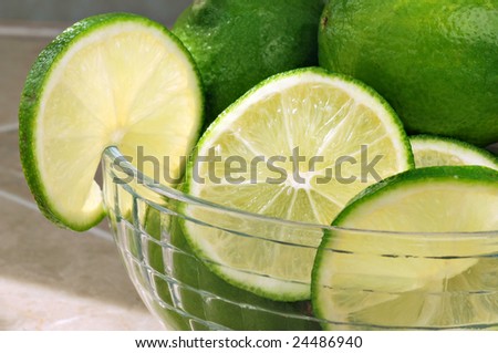Backlit slices of fresh limes in glass bowl with whole limes in background.  Macro with shallow dof.  Selective focus on center slice.
