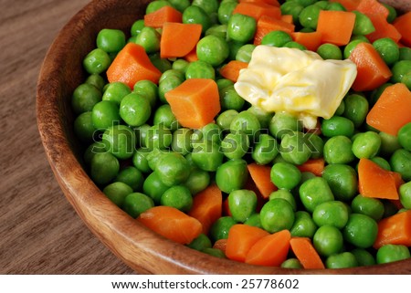 Bowl of freshly steamed peas and carrots with butter on wood background.  Macro with shallow dof.