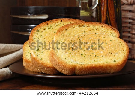 Rustic still life of freshly baked garlic bread seasoned with melted butter and herbs.  Olive oil and stoneware dishes in soft focus in background.