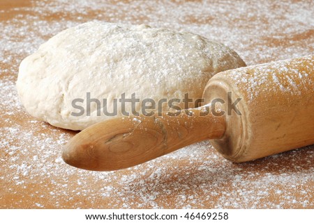 Classic wooden rolling pin with freshly prepared dough and dusting of flour.  Macro with shallow dof.