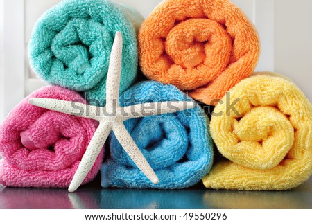 Colorful still life of towel rolls with white finger starfish on reflective surface.