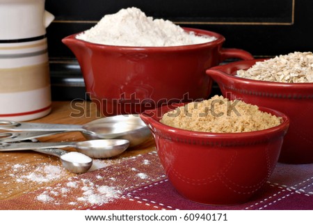 Baking still life of ceramic measuring cups and stainless steel spoons filled with ingredients.  Flour dusted in foreground.  Macro with shallow dof.