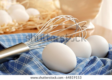Naturally sunlit still life of fresh eggs with whisk on kitchen table.  Eggs with raffia in background.  Closeup with shallow dof.