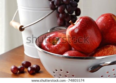 Freshly washed apples in colander with bucket of grapes in background.  Closeup with shallow dof.