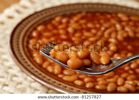 Hot delicious baked beans on fork with bowl of beans in soft focus in background.  Macro with extremely shallow dof.