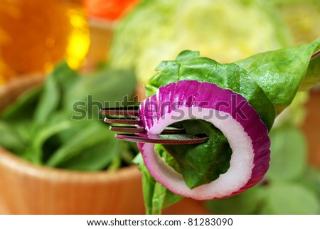 Fresh onion slice with lettuce and spinach on fork.  Bowl of baby spinach, head lettuce, carrots, and dressing in soft focus in background.  Macro with extremely shallow dof.