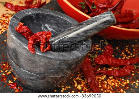Marble mortar and pestle with dried cayenne peppers being crushed into pepper flakes.  Macro with shallow dof.  Selective focus on pestle and peppers in mortar.