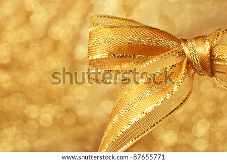 Shiny gold metallic bow against background of shimmery gold fabric (defocused) with copy space.