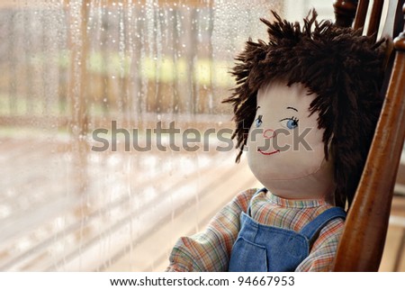 Handmade boy rag doll with cute sideways expression sitting alone next to a rainy window.  Closeup with shallow dof and copy space.