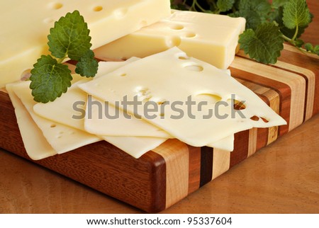Still life image of swiss cheese on wooden butcher block cutting board with herbs.  Macro with shallow dof.